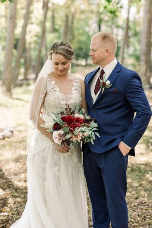 Elegant outdoor wedding photography featuring a lace wedding dress and navy blue suit with a stunning burgundy bouquet.