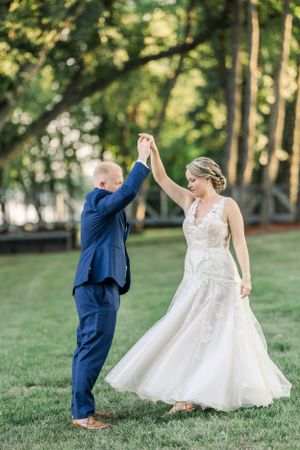 Wedding couple dancing on green lawn with classic navy suit and flowing white dress.