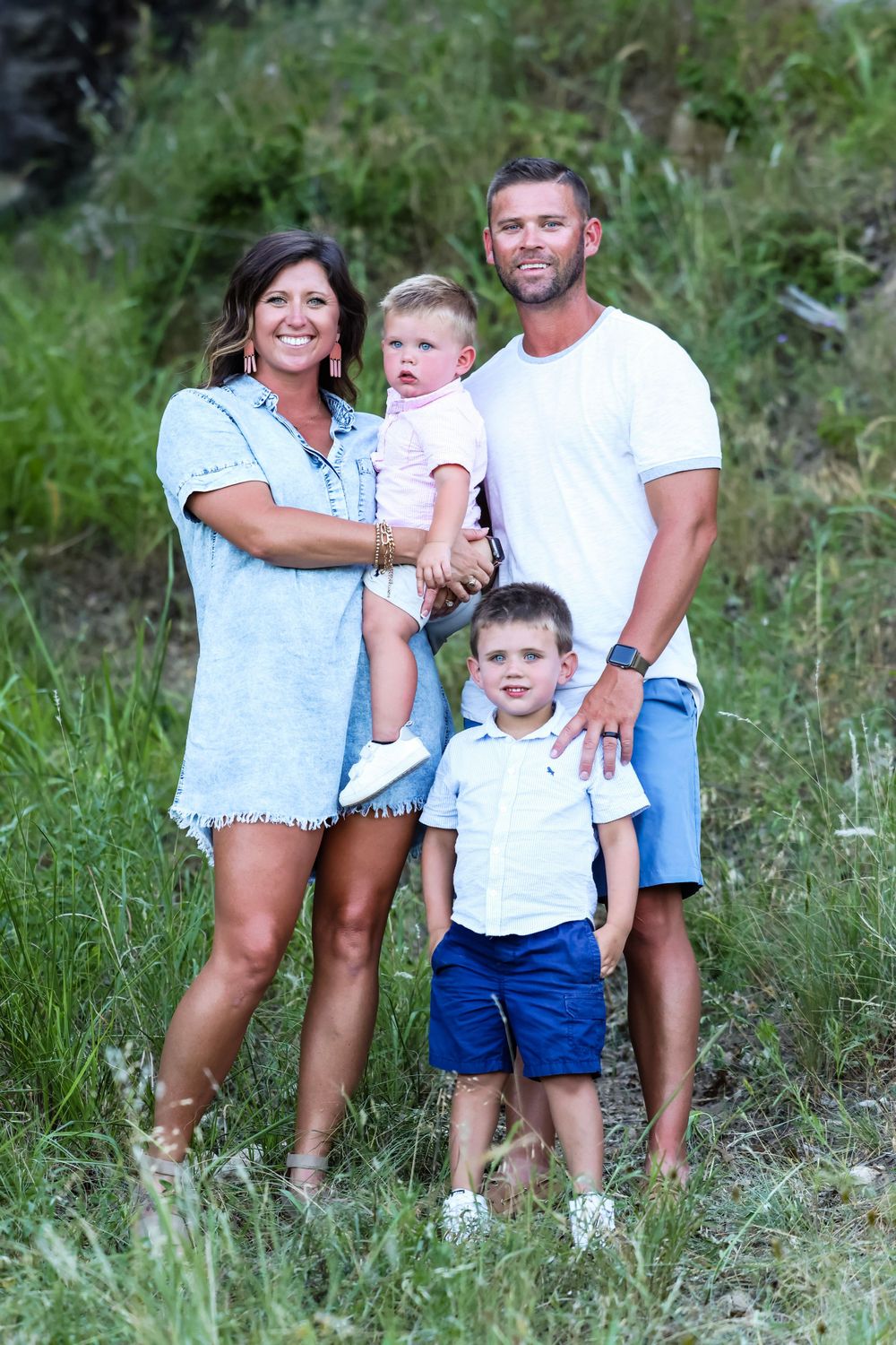 Casual family portrait in natural setting with tall grass and coordinated white outfits.
