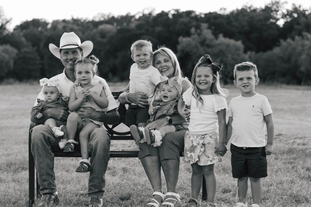 Black and white candid photo of group sitting casually on wooden bench in outdoor setting.