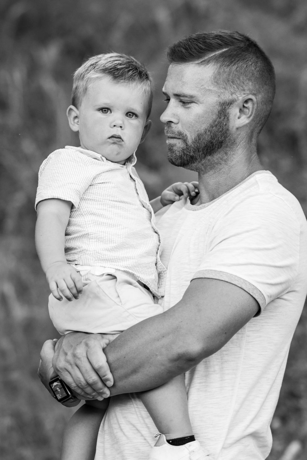 Black and white intimate portrait of parent and child in casual attire against natural backdrop.