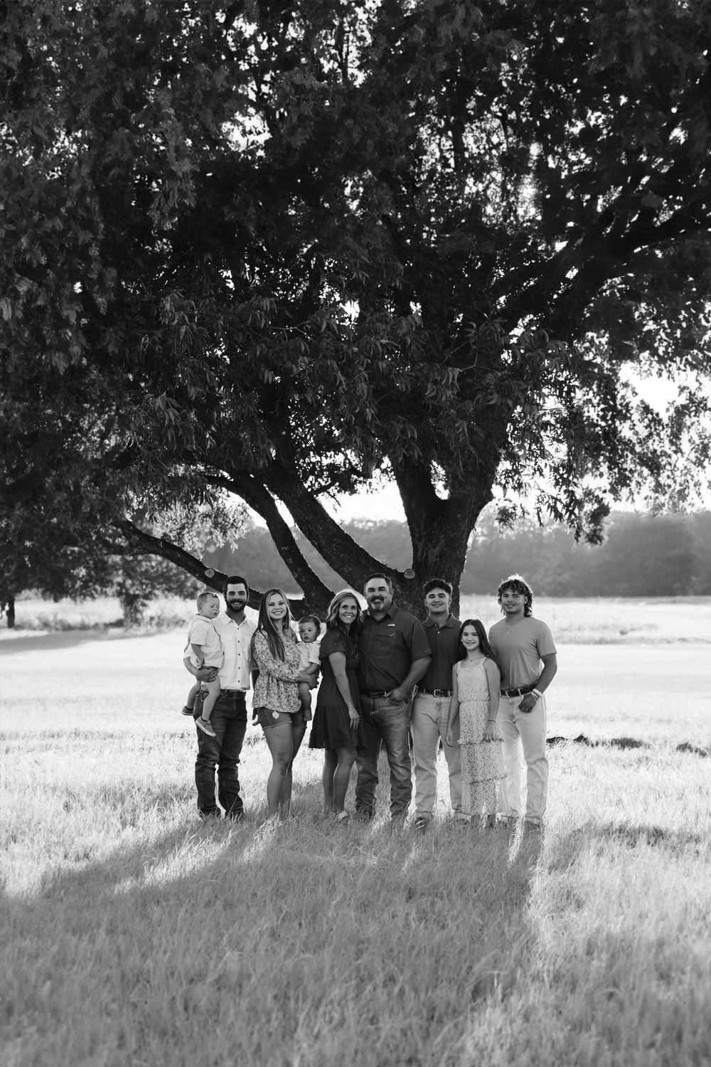 Black and white photo of family members gathering under a majestic tree in a field.