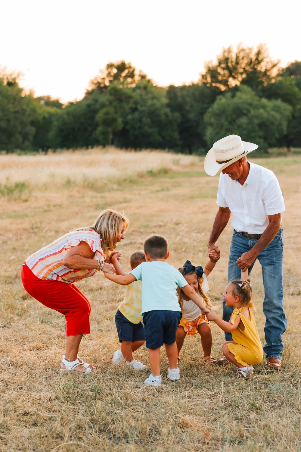 Playful intergenerational moment captured in golden field with cowboy hat and casual attire.