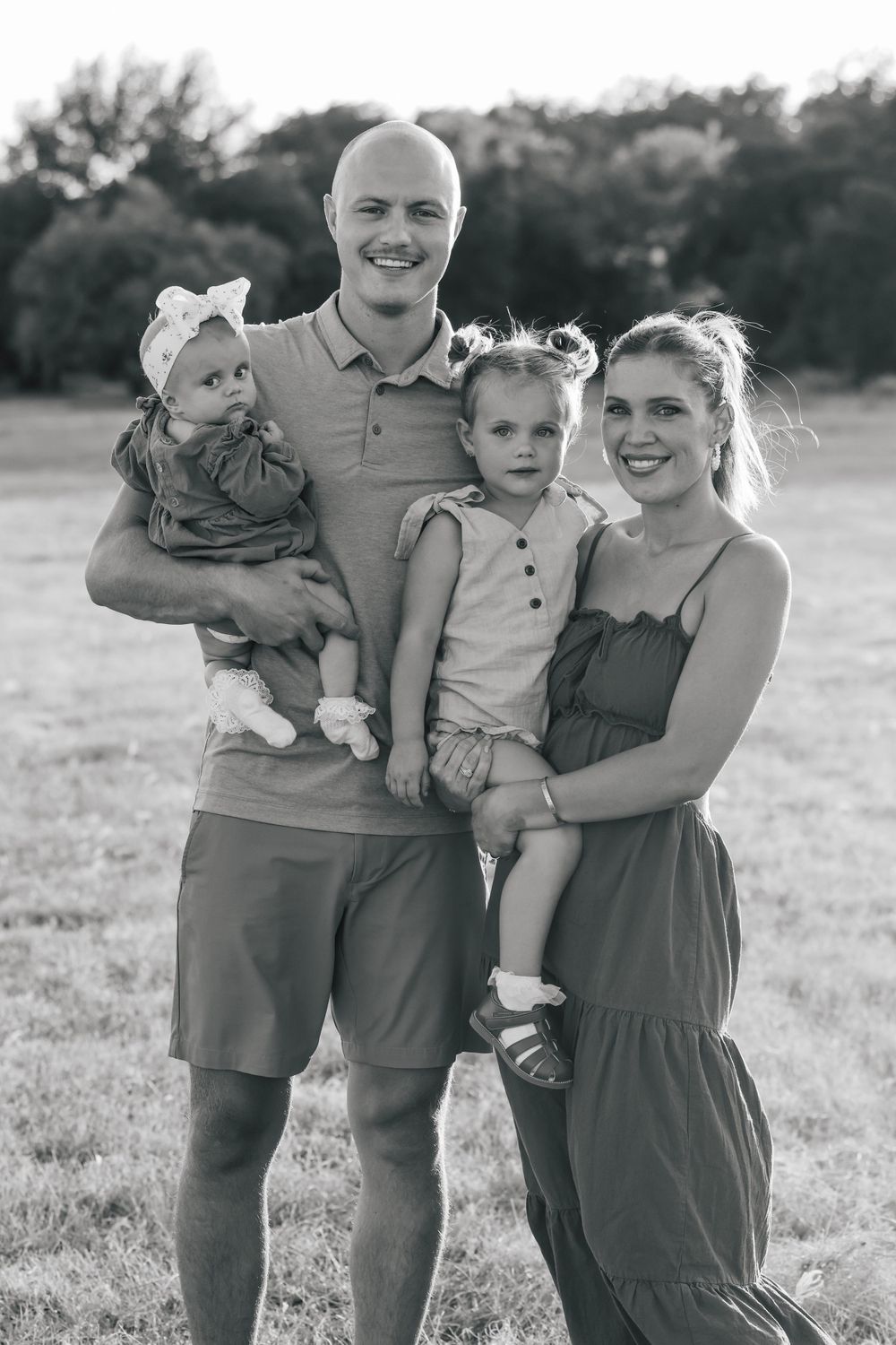 Black and white portrait of a young family together in a grassy field at sunset.
