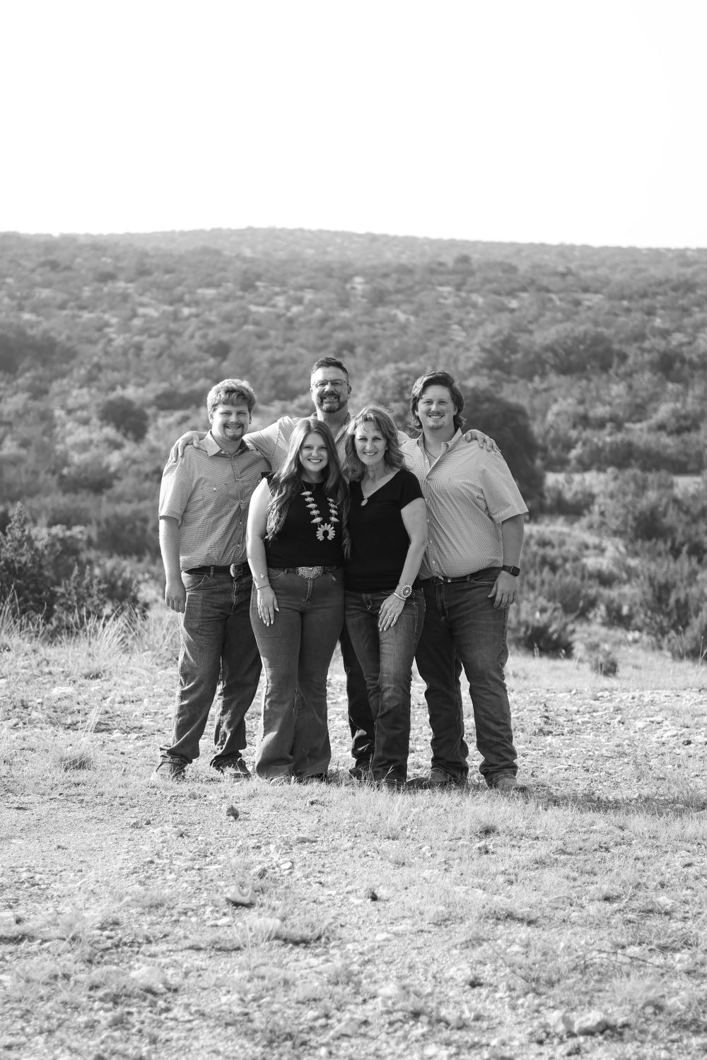Black and white group portrait of friends standing together on hilltop overlooking landscape.