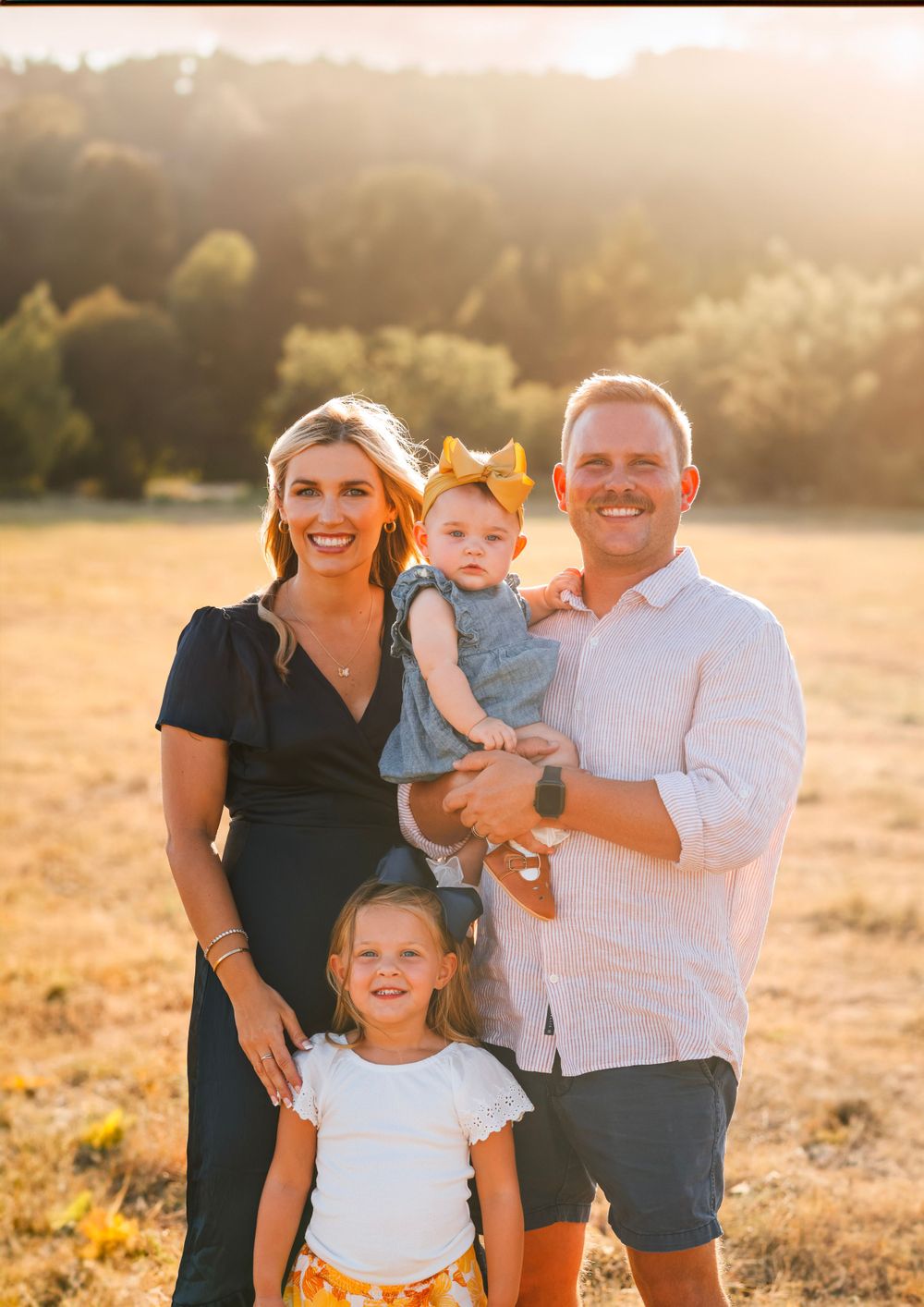 Family portrait at sunset with warm golden light in an open field.