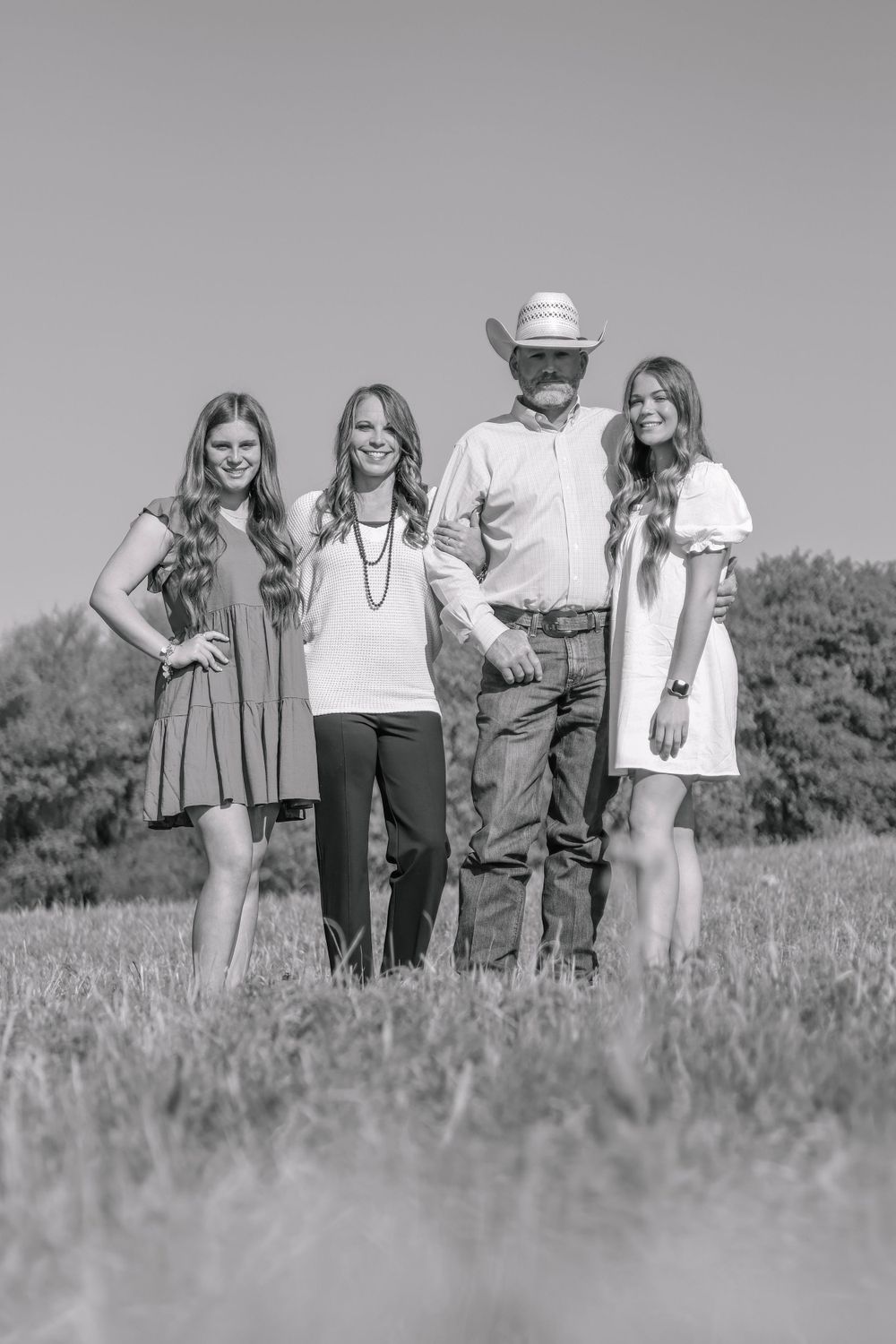 Black and white outdoor portrait of group standing in tall grass field wearing casual attire.