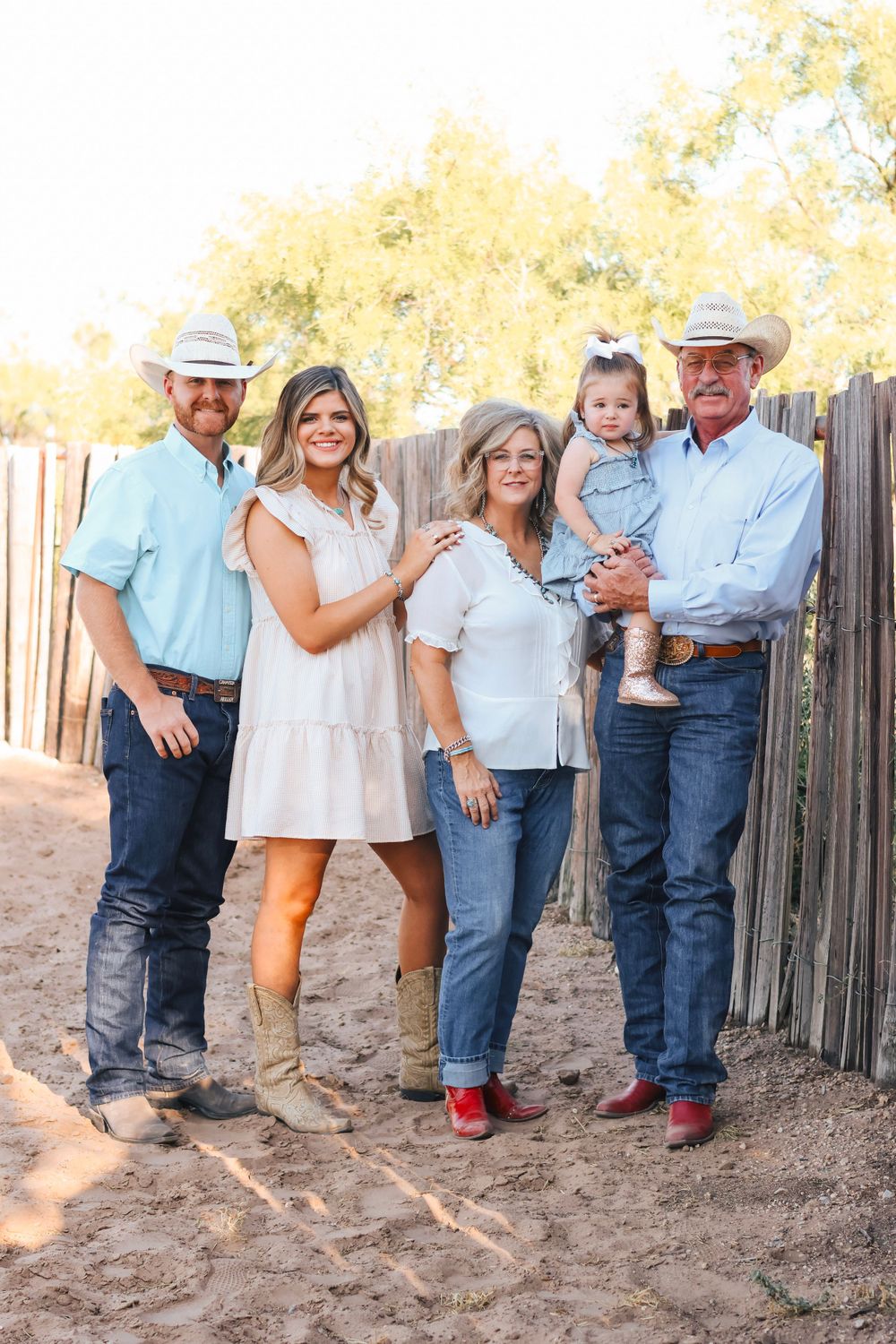 Multi-generational western family portrait against rustic fence in warm sunlight.