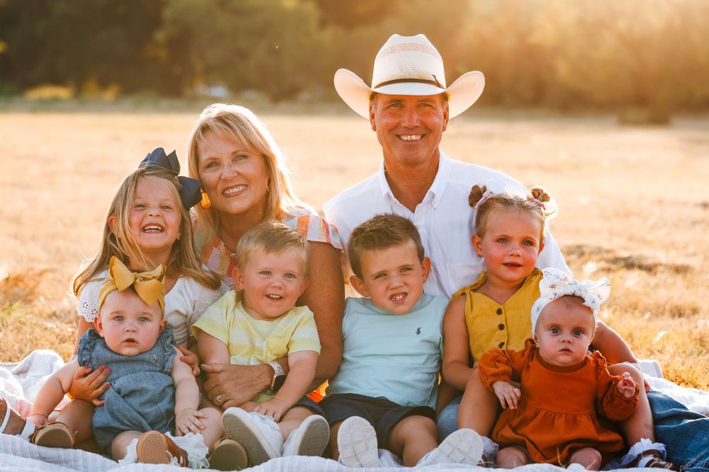 Cheerful group portrait sitting together outdoors in warm sunset light on blanket in field.