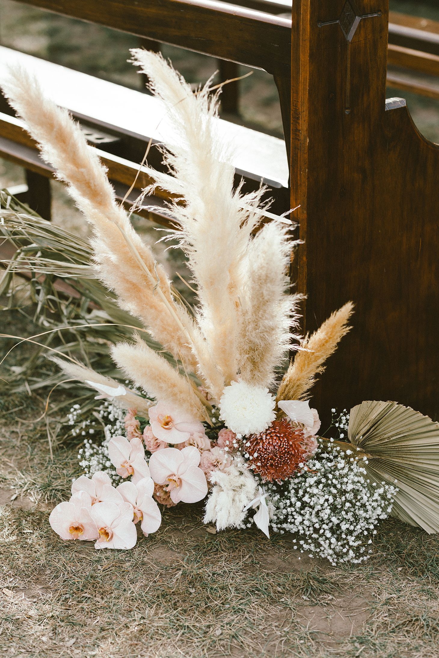 Wedding floral arrangement with pampas grass, dried palms and baby's breath against wooden church pews.