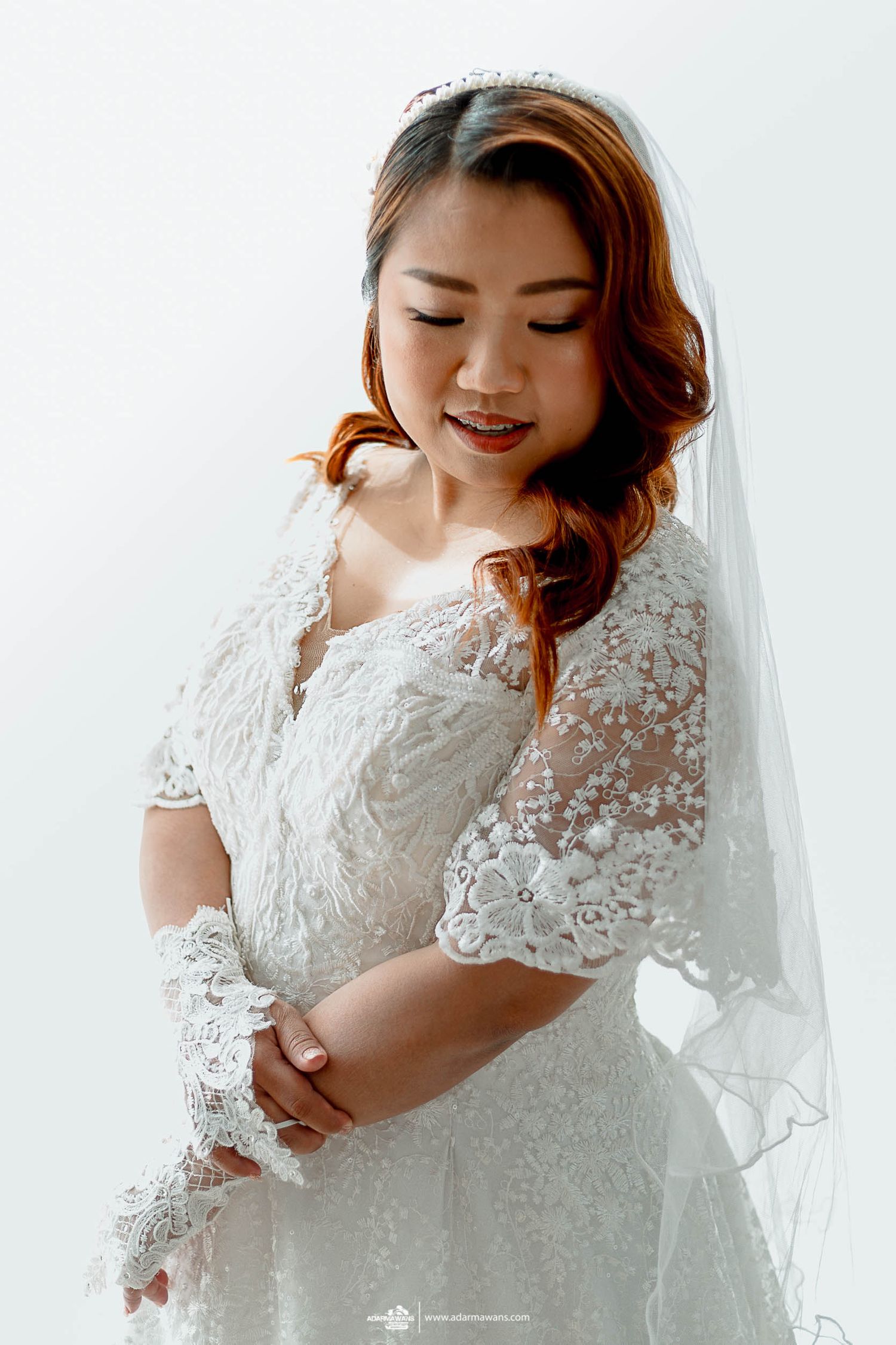A bride in a detailed lace wedding dress smiles softly while posing for a portrait.