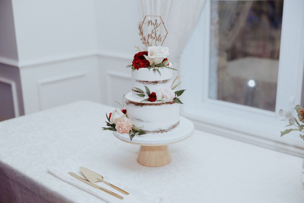 Elegant three-tier white wedding cake with red and pink floral decorations on display.