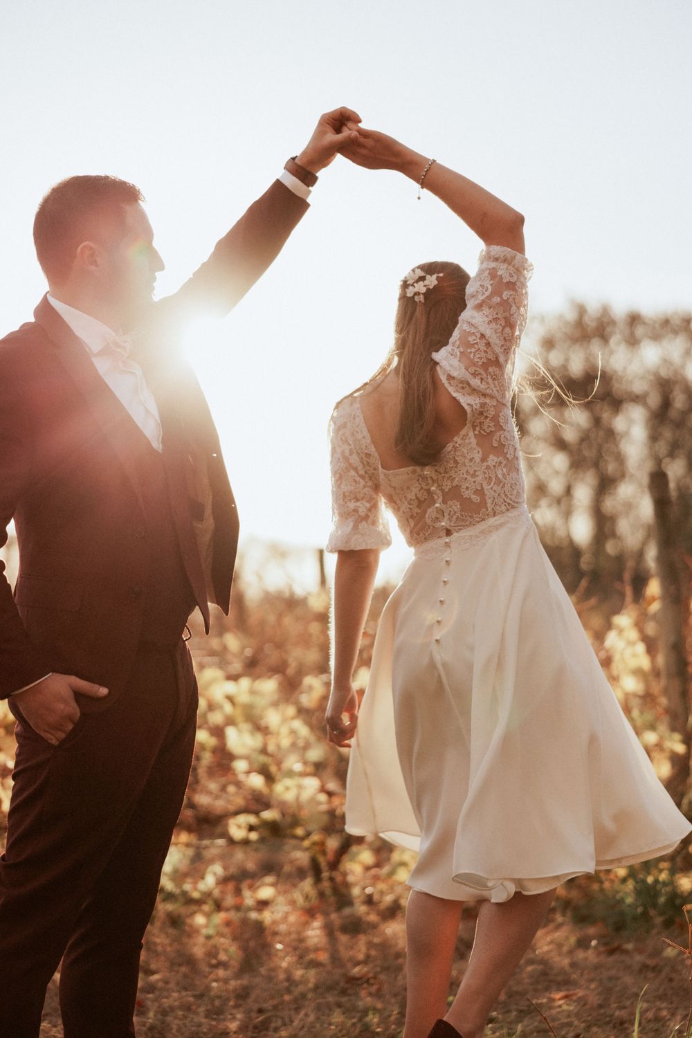 A backlit dance moment at sunset with the couple in burgundy and white wedding attire.