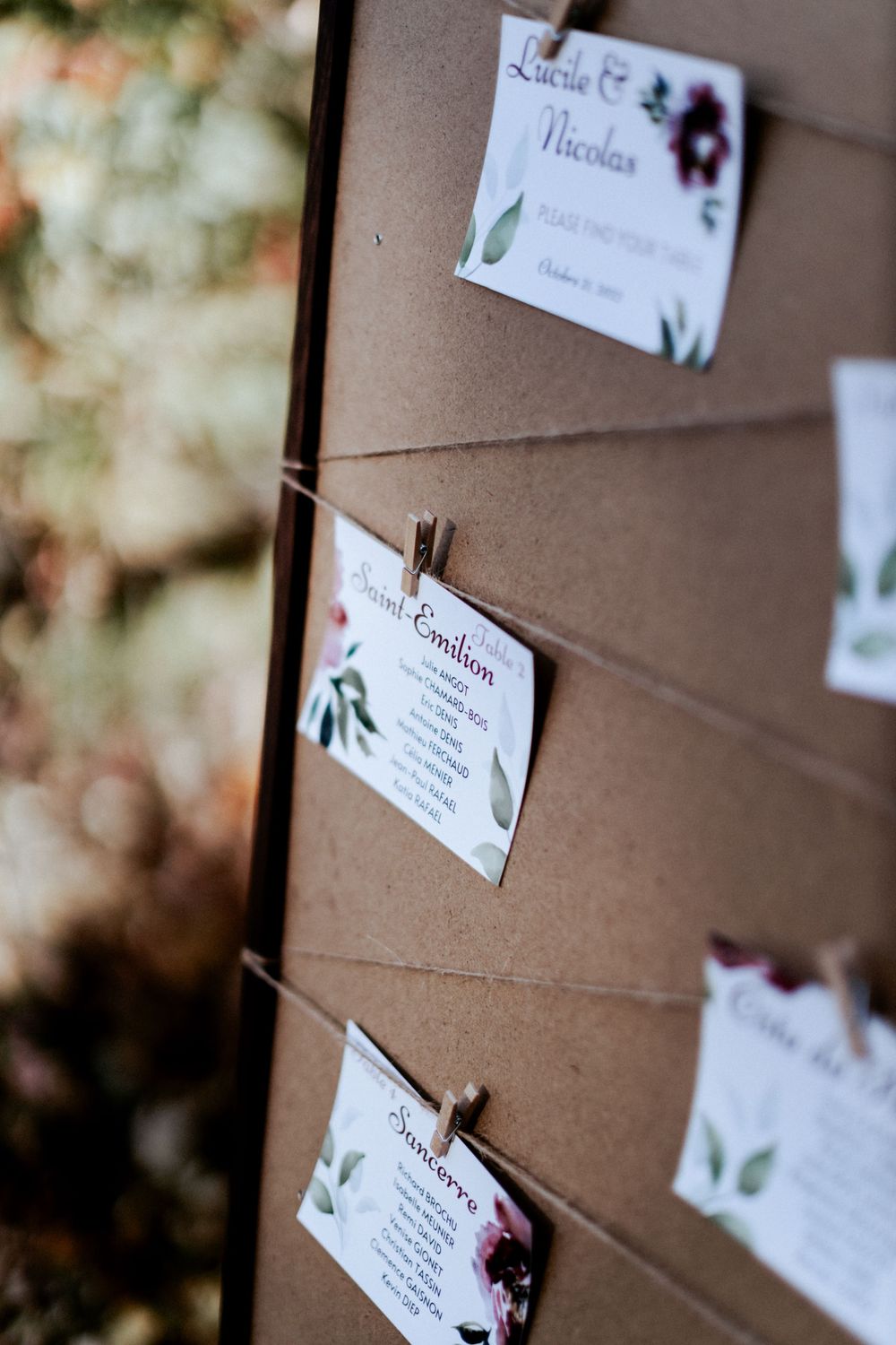 Wedding seating cards with floral designs clipped to string against a brown backdrop.