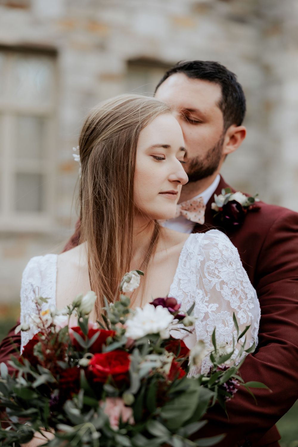 An intimate wedding portrait with burgundy and white florals in soft natural light.
