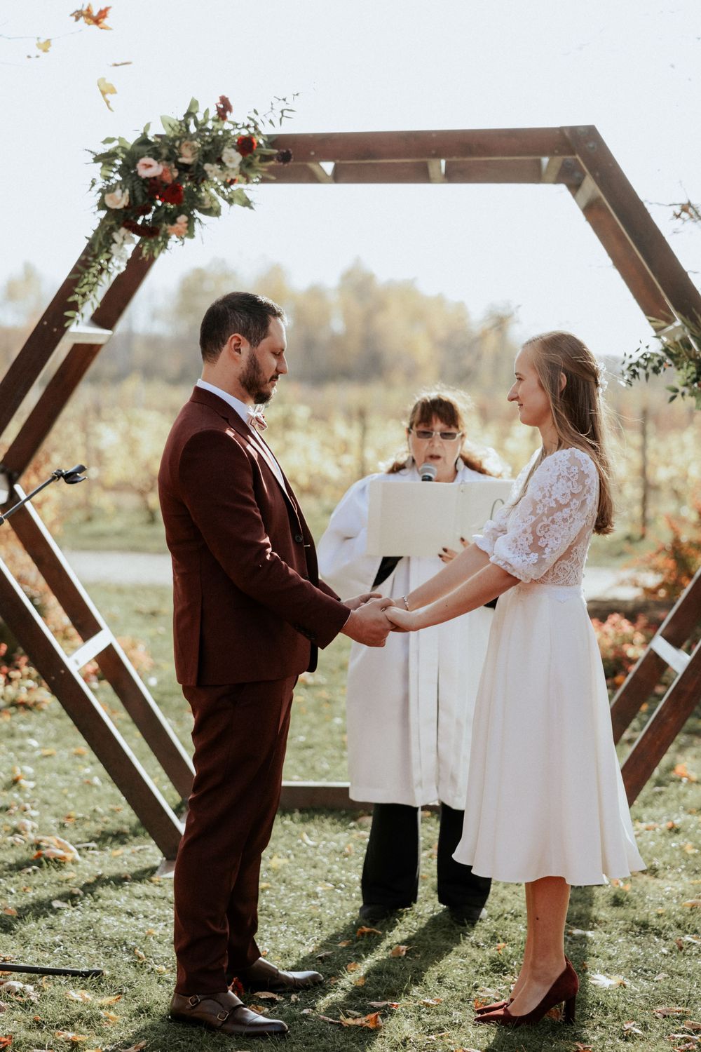 An intimate wedding ceremony under a hexagonal arch with burgundy and white floral decorations.