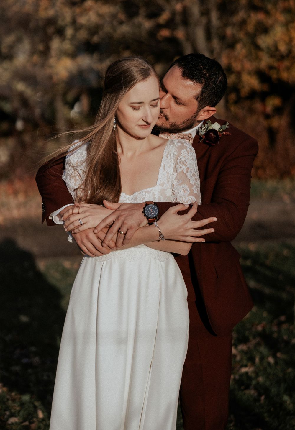 A tender moment between newlyweds with the bride in a lace dress and groom in burgundy suit.