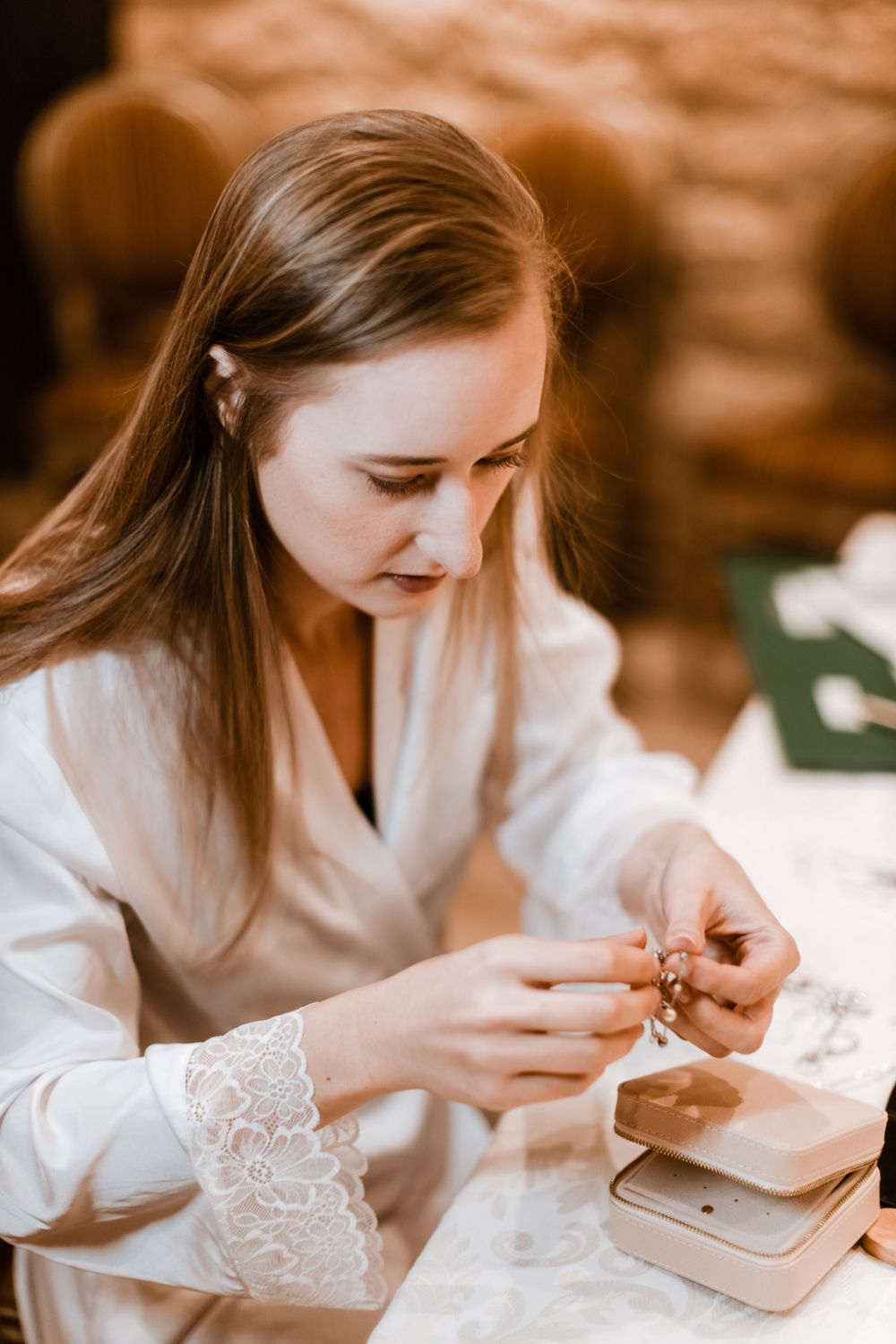 A person in a white lace robe carefully prepares jewelry on their wedding morning.