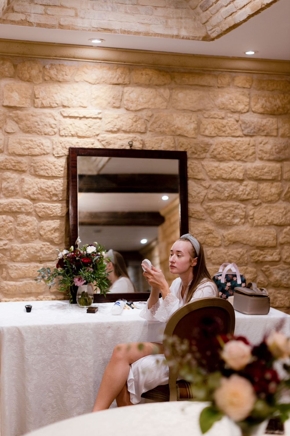 A person sitting at an elegantly decorated table with floral arrangements and a mirror in a stone-walled room.