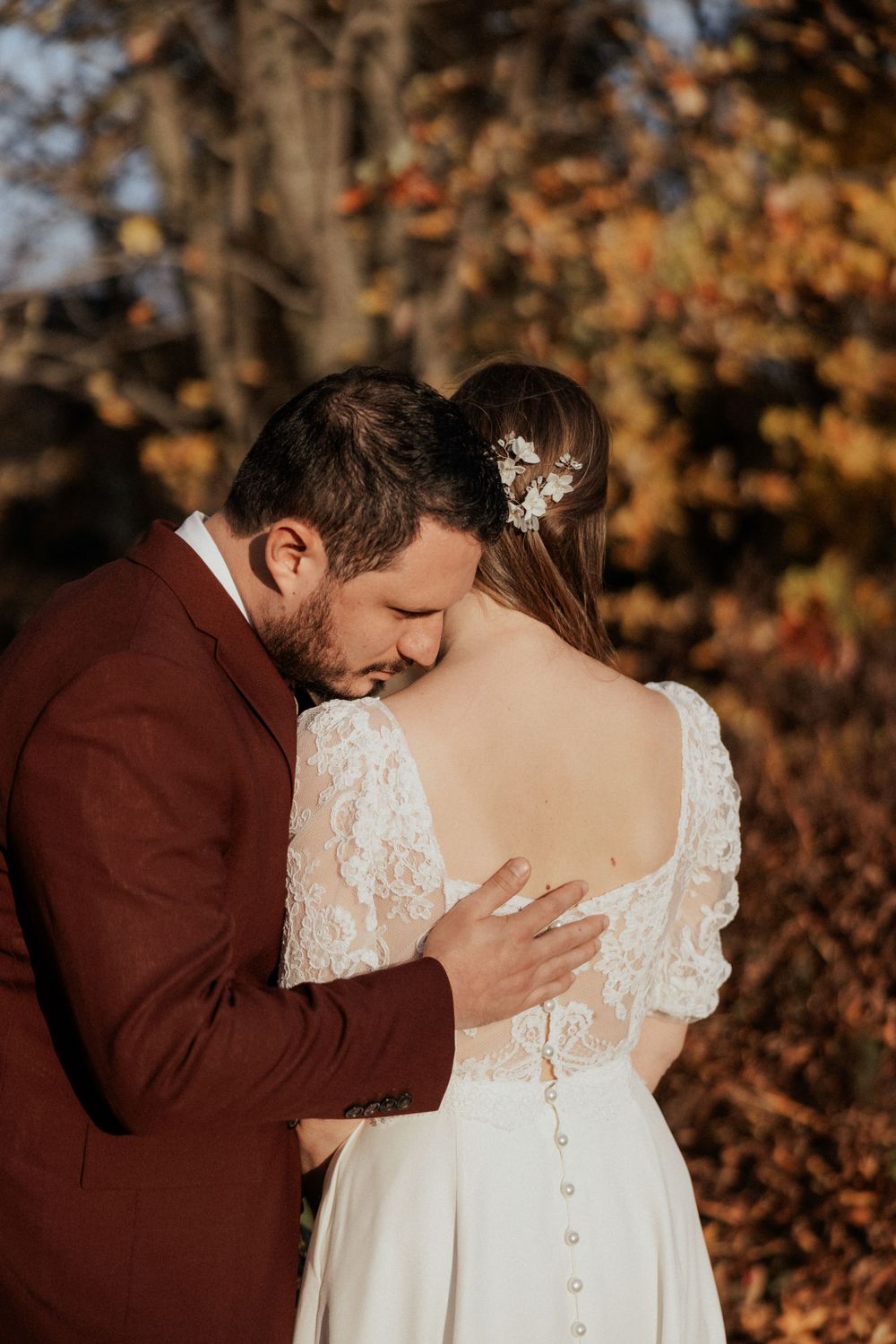 Romantic wedding portrait showing couple embracing outdoors with autumn foliage in background.