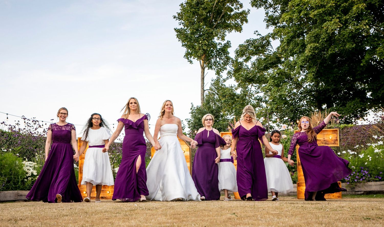 Wedding party in purple dresses posing together on grassy hillside.