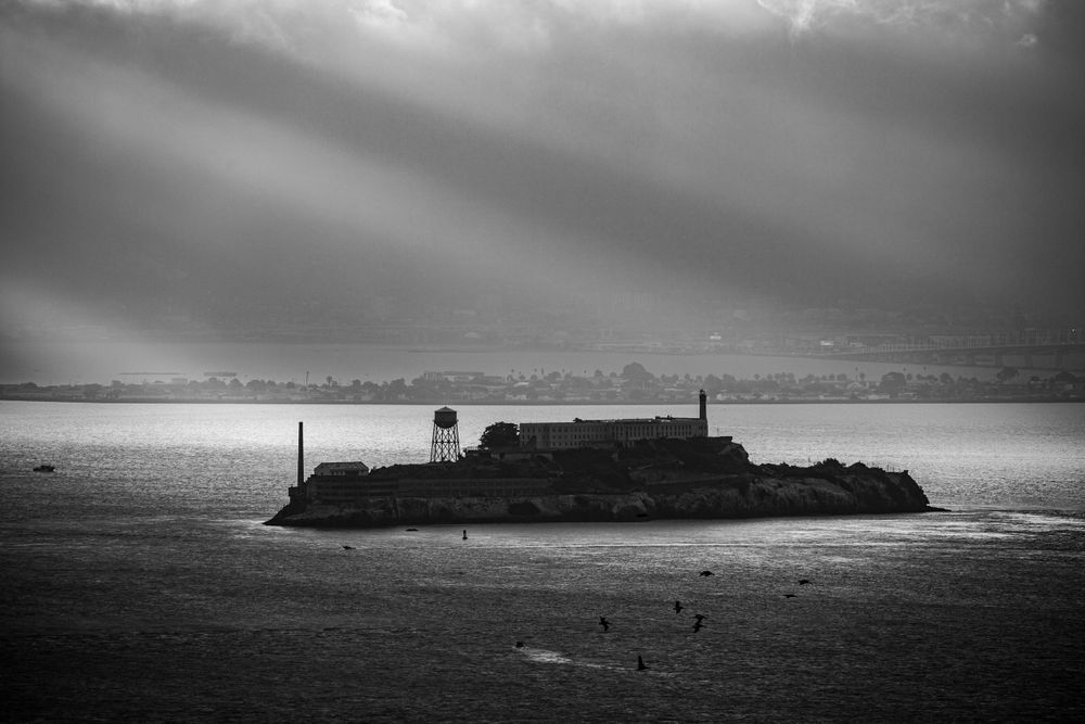 Dramatic black and white view of Alcatraz Island under moody storm clouds in San Francisco Bay.