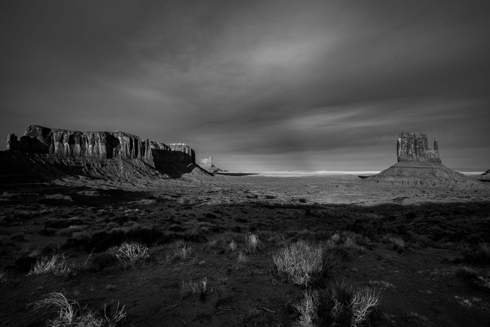 Desert mesas and rock formations silhouetted against moody sky in Monument Valley.