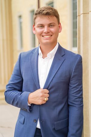 Graduate in a navy blue suit poses confidently against a light colored building exterior.