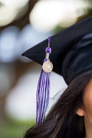 Close-up of purple and silver graduation tassel hanging from black mortarboard cap.