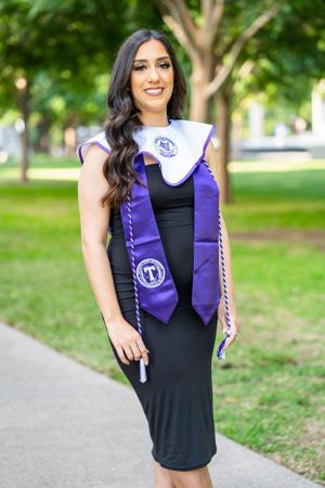 Graduate in black dress and purple stole poses on campus during graduation photoshoot.