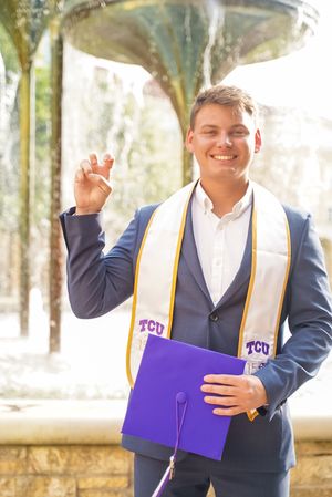 Graduate in TCU stole celebrates with diploma and victory gesture.