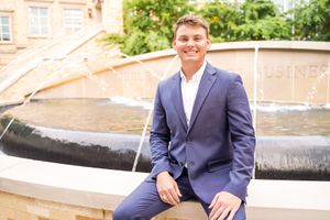 Graduate in navy suit poses on stone steps during outdoor photo session.