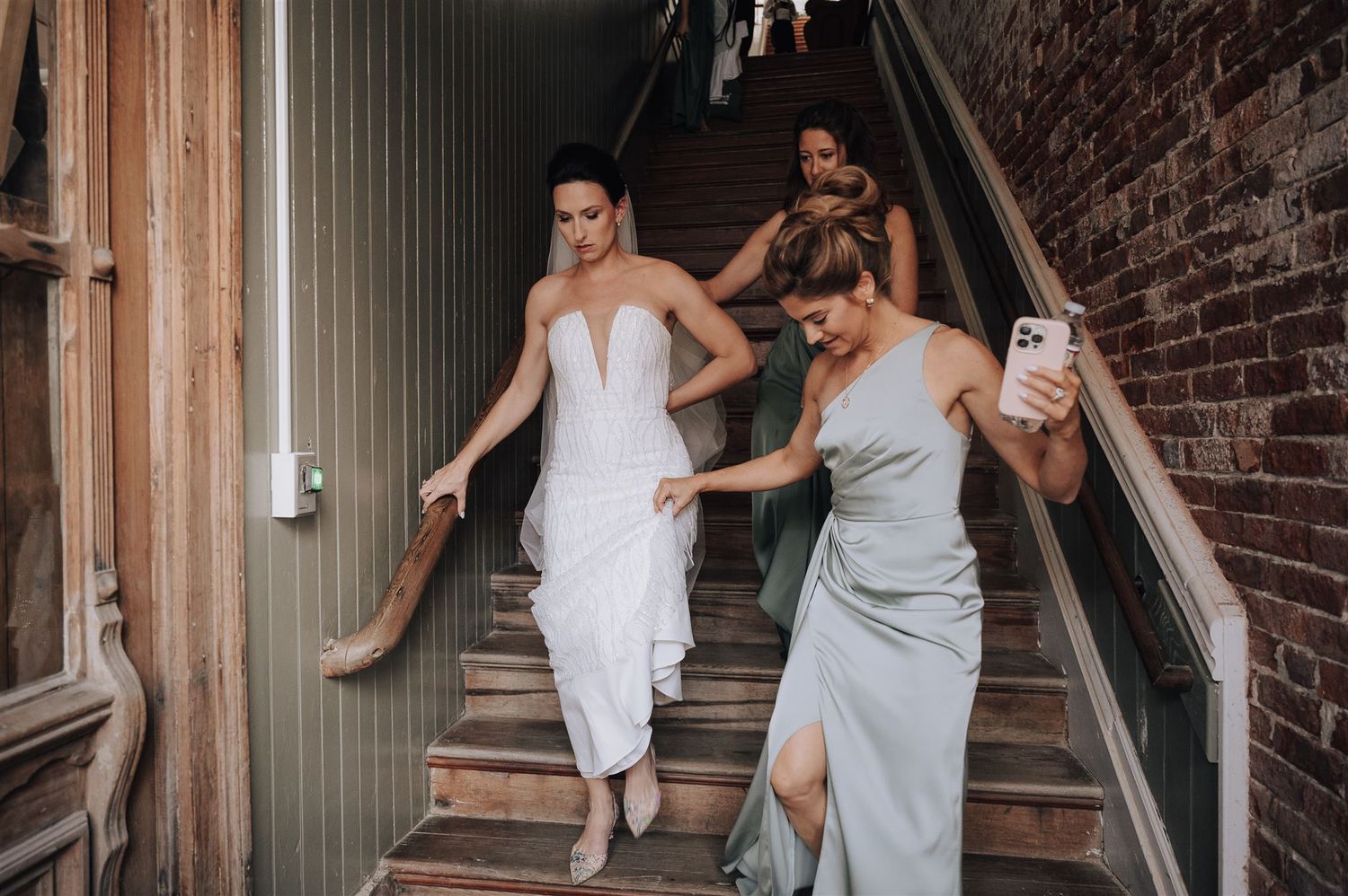 Wedding party descends stairs while taking photos on their phones.