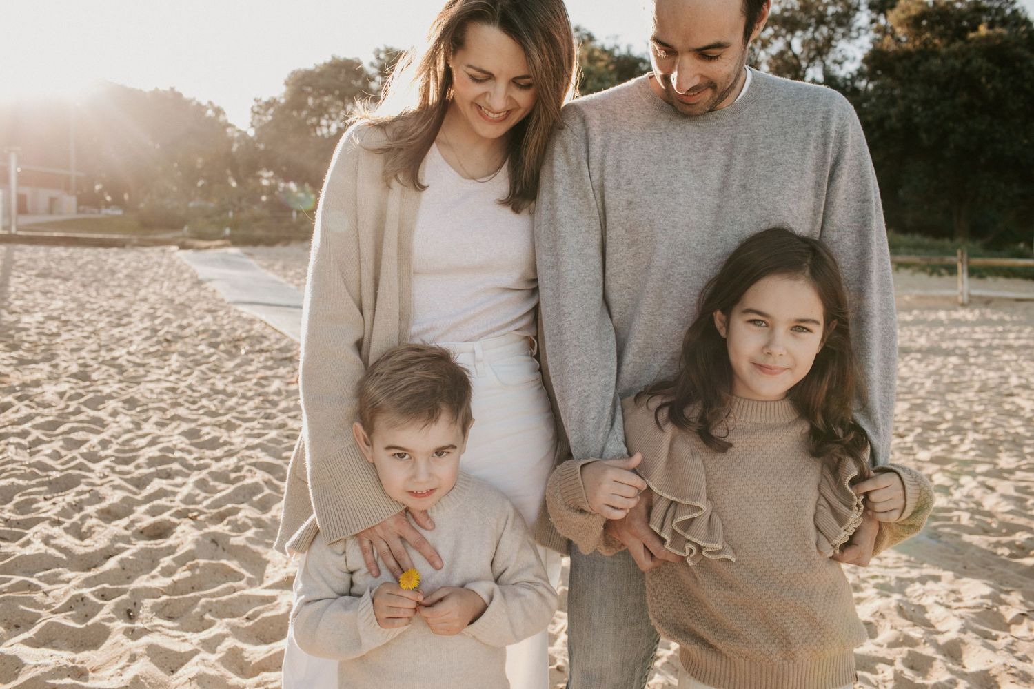 Happy family of four posing together on a sandy beach at golden hour.