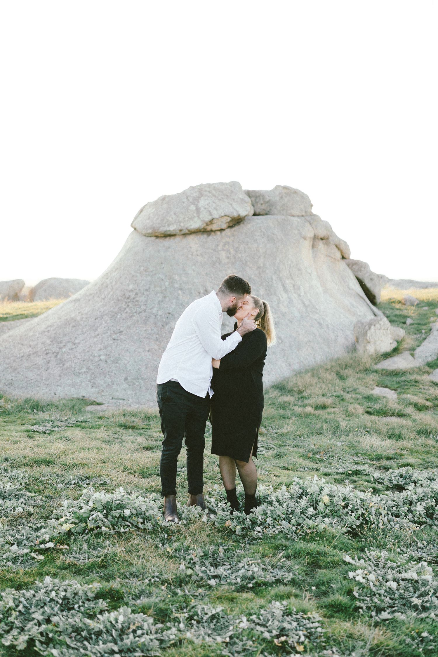 A romantic moment captured in front of a stark white rock formation at golden hour.