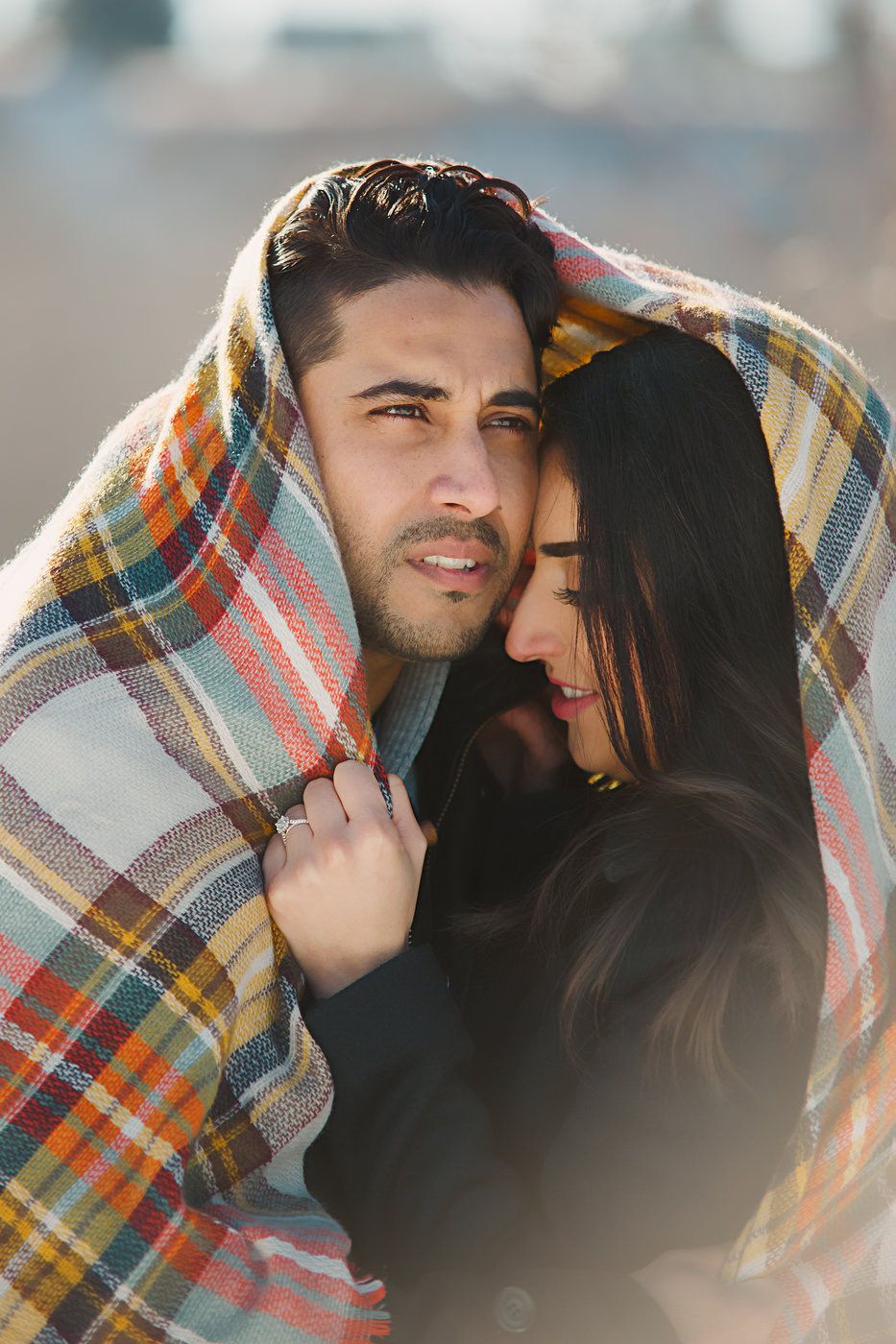 Romantic couple wrapped in plaid blanket sharing intimate moment outdoors.