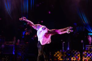 Dancer executes a dramatic leap on stage under purple lighting effects.