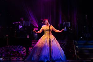Singer performing in an elegant yellow ballgown under purple stage lights.