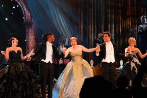 Group performers dancing in elegant formal wear during a theatrical production on stage.