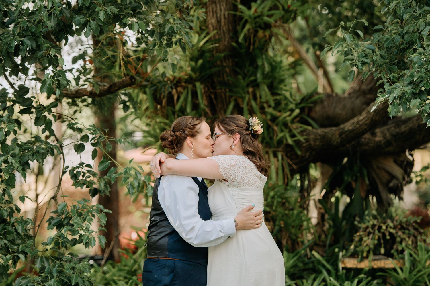 A romantic embrace under a canopy of trees in a garden wedding setting.