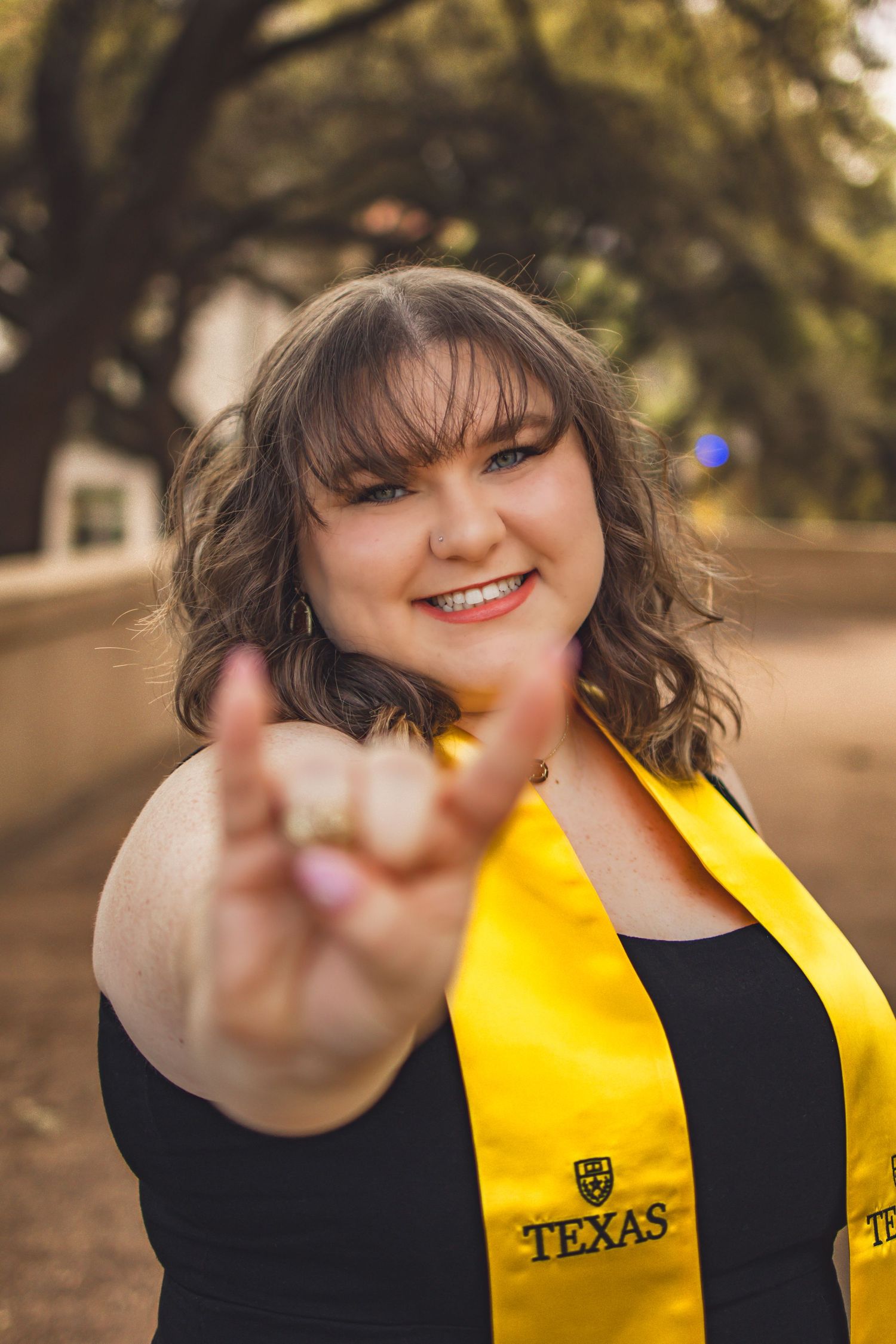 Graduate in yellow stole from Texas university gives peace sign to camera.