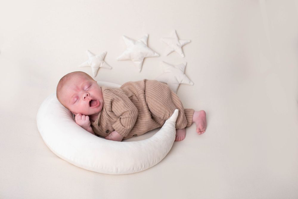 Sleeping newborn baby yawning in a white crescent moon prop with star decorations on white background.