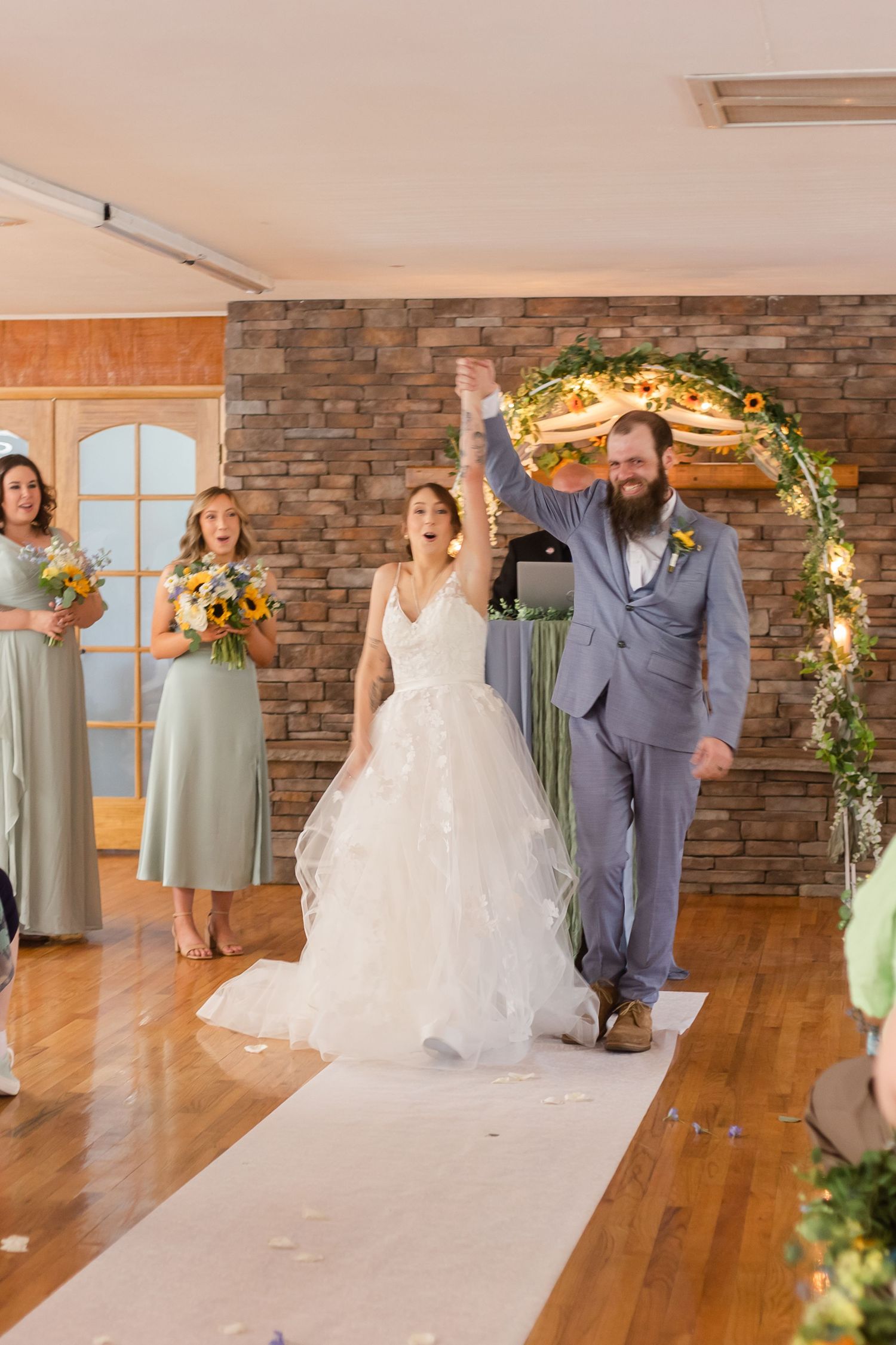 Wedding party members walking and posing in an elegant reception hall with hardwood floors.