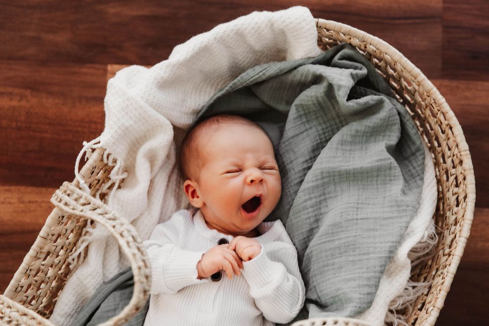 A baby yawns as he lies in a light-colored straw Moses basket