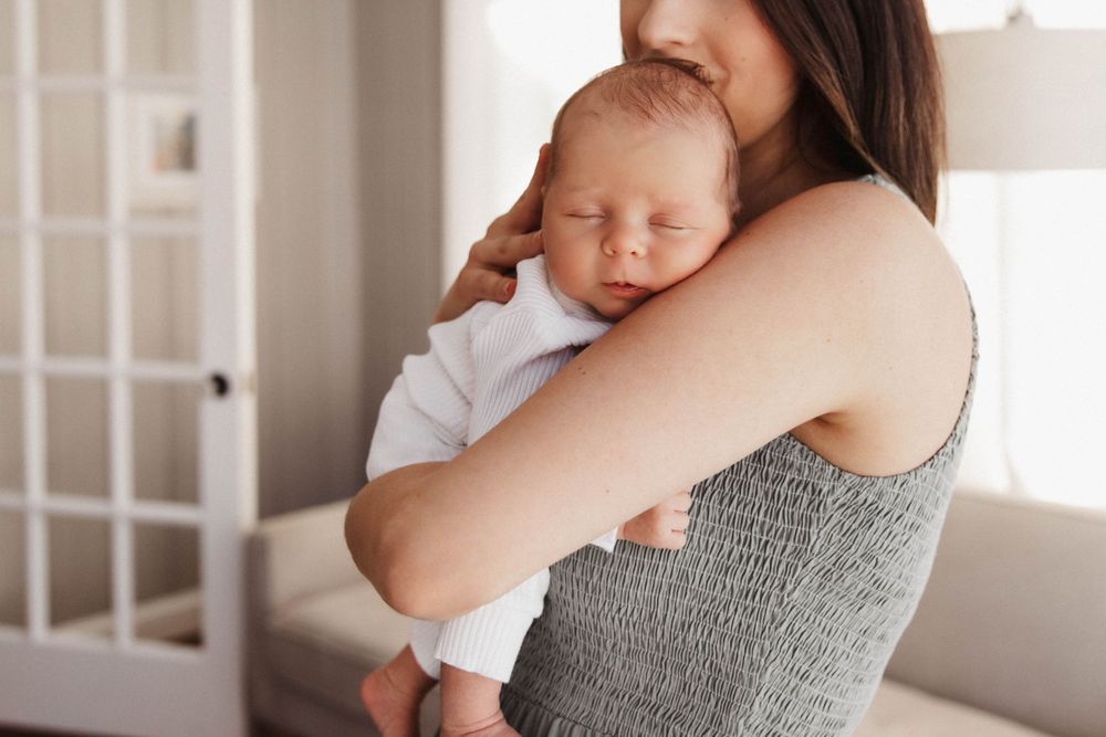 A newborn baby sleeps while resting on his mother's shoulder