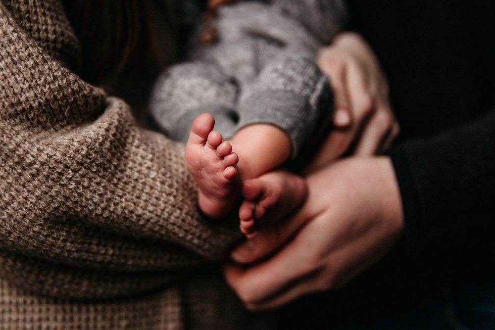 Detail photo of newborn baby's toes as he is held by both his mom and dad. Dad's hands rest on mom's arm.
