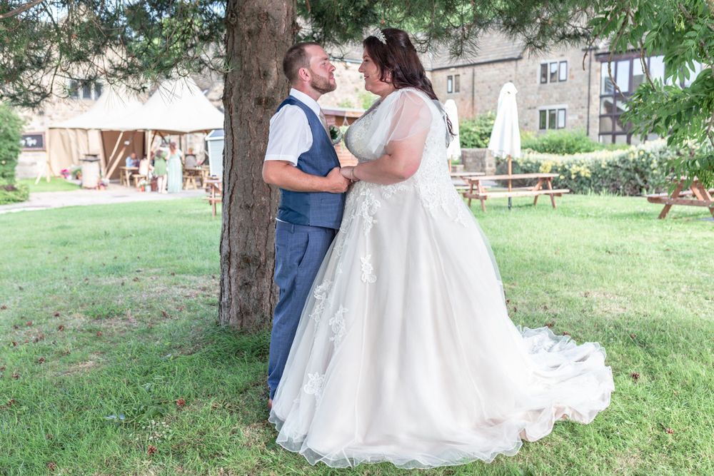 Romantic outdoor wedding photos taken under tall trees on a sunny day.