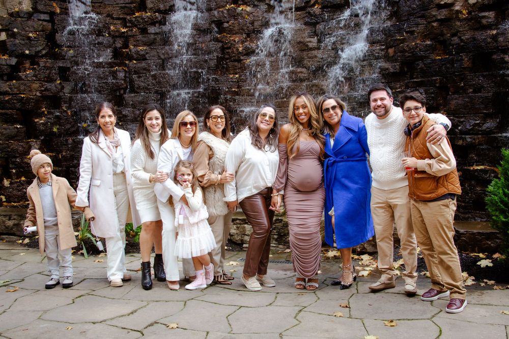 A group in coordinated neutral tones poses together against a rustic stone wall.