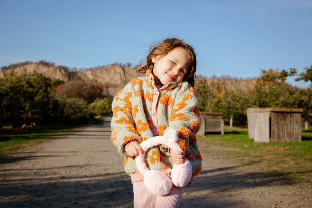 A baby in orange floral attire is held against a mountain backdrop at sunset.