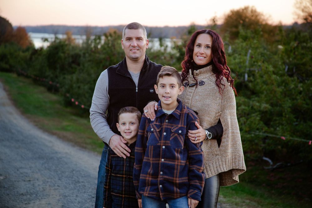 Family portrait taken outdoors during sunset with autumn scenery in background.
